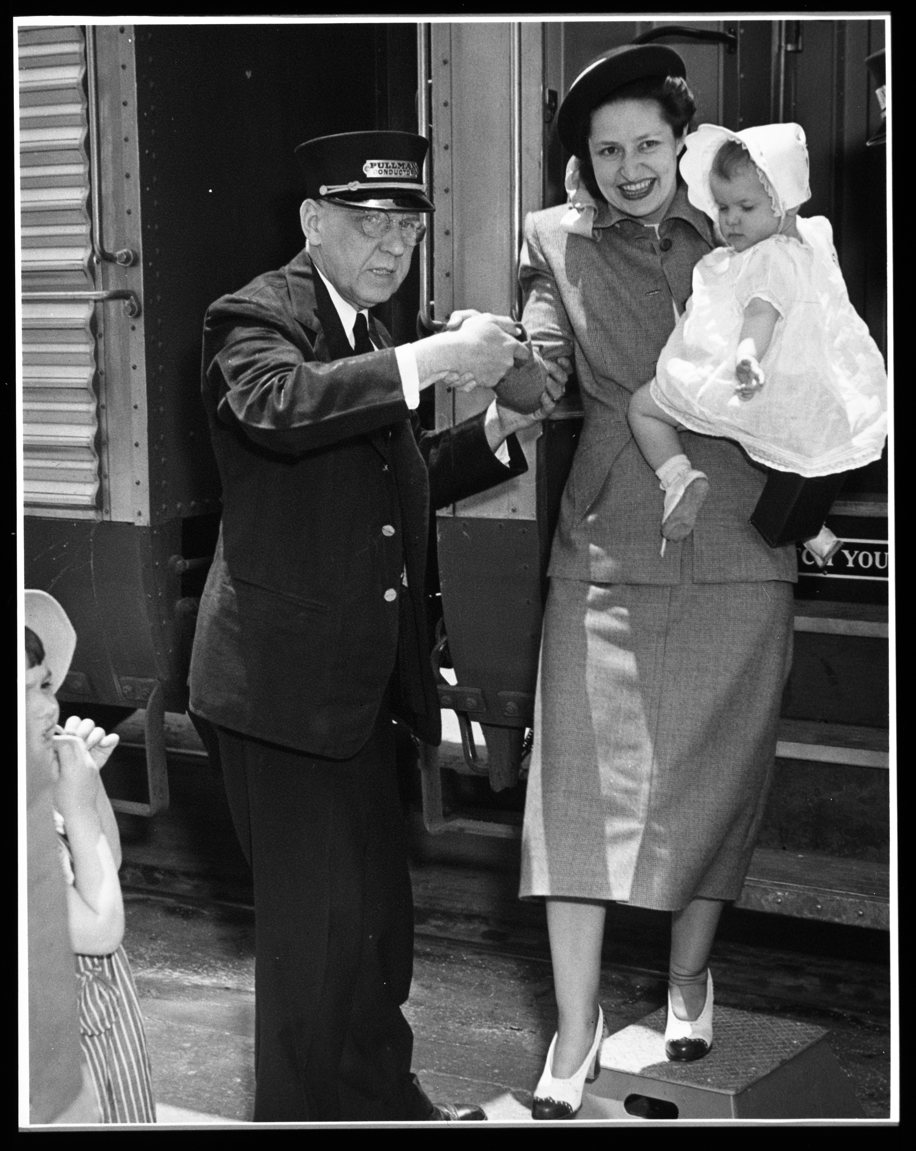 Lady Bird Johnson being helped off a train by a conductor while holding her baby daughter Luci